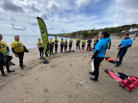 A large group of people stood on the beach in wetsuits and Cornwall Wildlife Trust rashvests