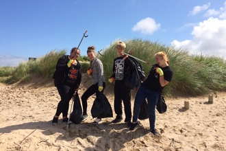 Young people pose on a beach next to dunes, with litter pickers and bin bags