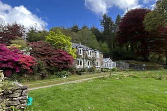 A sunny shot of The Lodge. A farmhouse can be seen in the background, surrounded by an array of brightly-coloured trees and shrubs.