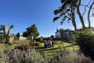 A sunny photograph of Meadowside farmhouse and garden, featuring a variety of shrubs and trees.