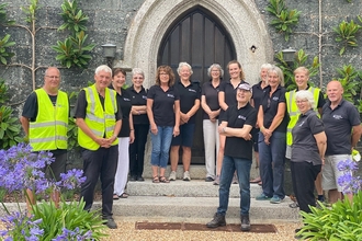 A group of Cornwall Wildlife Trust volunteers smiling outside a door, surrounded by purple flowers.
