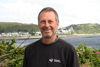 Image of a person smiling with the sea and coastline behind