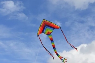 a rainbow striped kite flying against a blue sky with a few white fluffy clouds