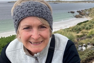 Image of a person smiling with penguins and the sea in the background