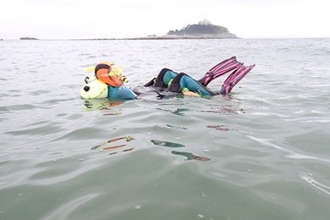 A snorkeller floats on their yellow towfloat in the sea, with St Michael's Mount in the background