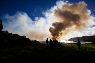 Silhouette of people around an outdoor fire, as the smoke blocks out the sun
