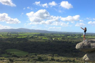 A woman, with arms outstretched, stood on the edge of a rock overlooking a vast landscape