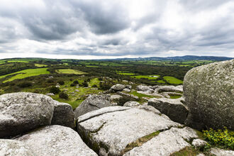 Landscape view from on top of Helman Tor, with boulders in the foreground and fields in the background