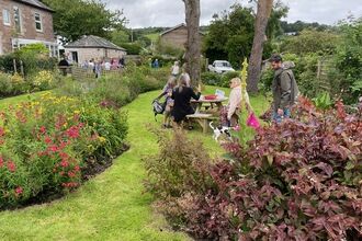 People sat round a picnic bench on a lawn surrounded by flowers