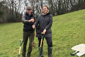 Two people posing with young tree and shovels