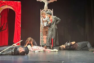 A scene from the choughs panto performance, An appointment with MacDeath, is shown with characters lain on the floor while other characters watch over them 