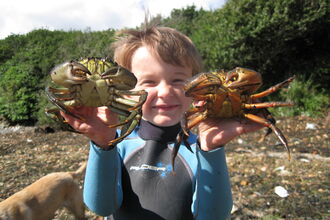 Young boy demonstrating how to correctly hold two crabs, one in each hand