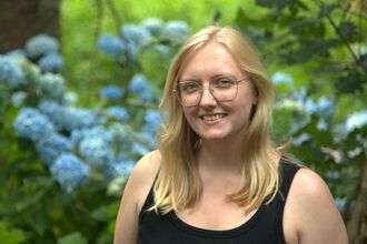 Image of a person smiling with a background of trees and flowers