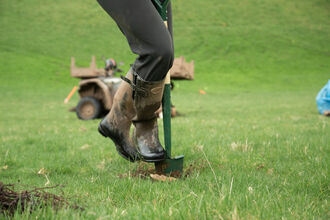 A close-up of a person's legs, wearing muddy wellies and digging into the ground with a shovel