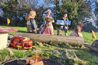 Children watching a lady dressed as a fairy read a children's book.
