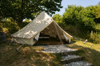 A white bell tent, surrounded by trees, with the doors open to show a double bed inside
