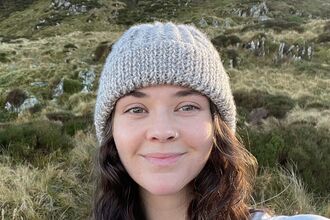 A person smiling and standing in front of grasses and rocks 