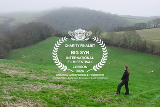 Project manager alison from Cornwall wildlife trust surveys the landscape of tree planting and temperate rainforest restoration ahead of her while a logo banner anounces that cornwall wildlife trust is a finalist in the big syn film festival 
