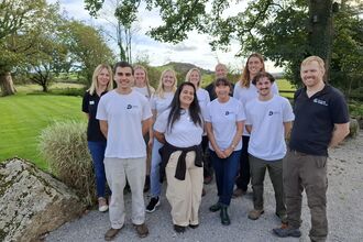 A group of Cornwall Wildlife Trust staff stood smiling with Helman Tor in the distant background