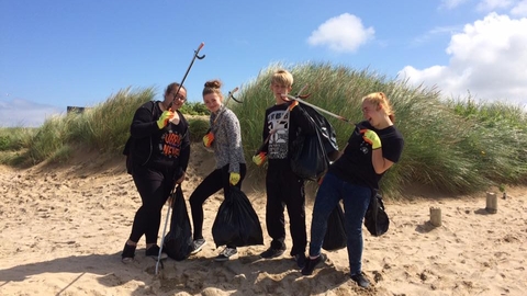 Young people pose on a beach next to dunes, with litter pickers and bin bags