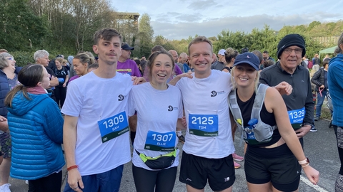 A group of four runners standing in a line, smiling at the camera.