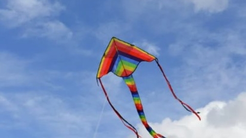 a rainbow striped kite flying against a blue sky with a few white fluffy clouds