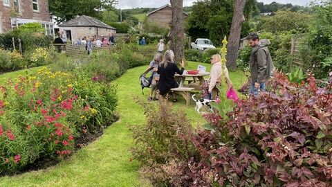 People sat round a picnic bench on a lawn surrounded by flowers