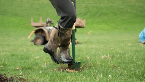 A close-up of a person's legs, wearing muddy wellies and digging into the ground with a shovel