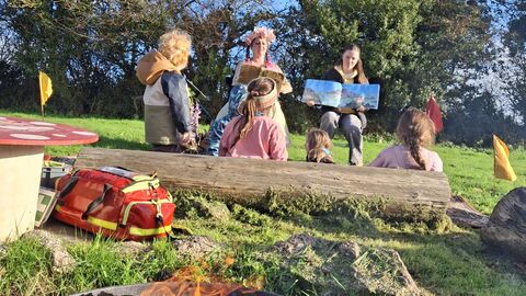 Children watching a lady dressed as a fairy read a children's book.