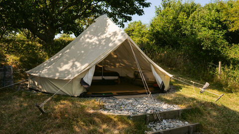A white bell tent, surrounded by trees, with the doors open to show a double bed inside