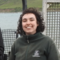 A woman with dark curly hair in a green fleece smiles at the camera