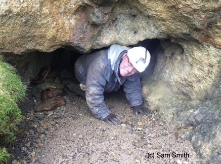 A man crawls out of a cave, smiling at the camera