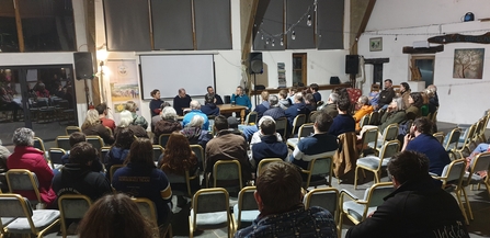A seated conference hall filled with people listening to three speakers