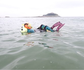A snorkeller floats on their yellow towfloat in the sea, with St Michael's Mount in the background