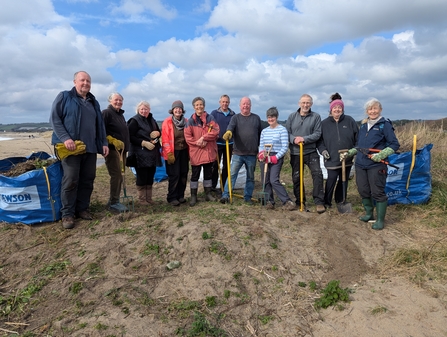 A group of sand dune volunteers stood around facing the camera, some holding spades 