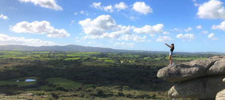 A woman, with arms outstretched, stood on the edge of a rock overlooking a vast landscape