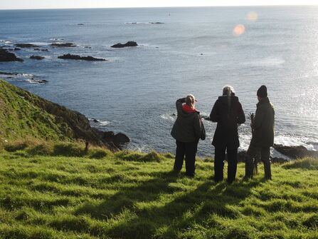 Three people stood on the coast looking out to sea on a sunny day