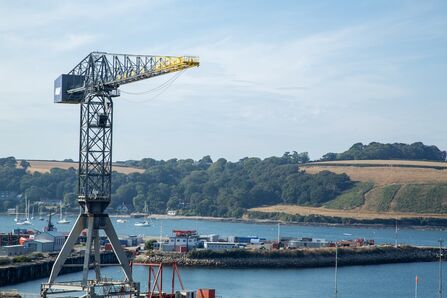 Port crane overlooking Falmouth Docks, with water, boats, and rolling green hills in the background.