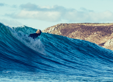 Surfer on wave, cliffs visible in the background