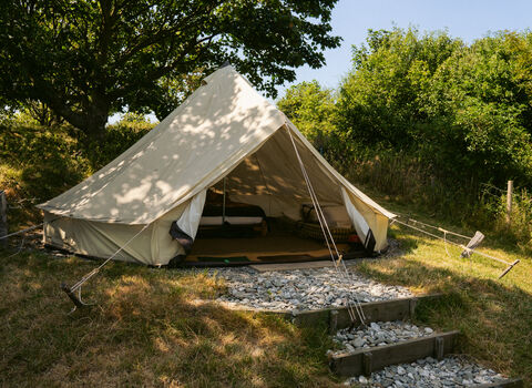 A white bell tent, surrounded by trees, with the doors open to show a double bed inside