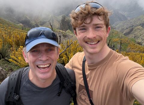 Two men smile at the camera with a foggy moorland scene behind them